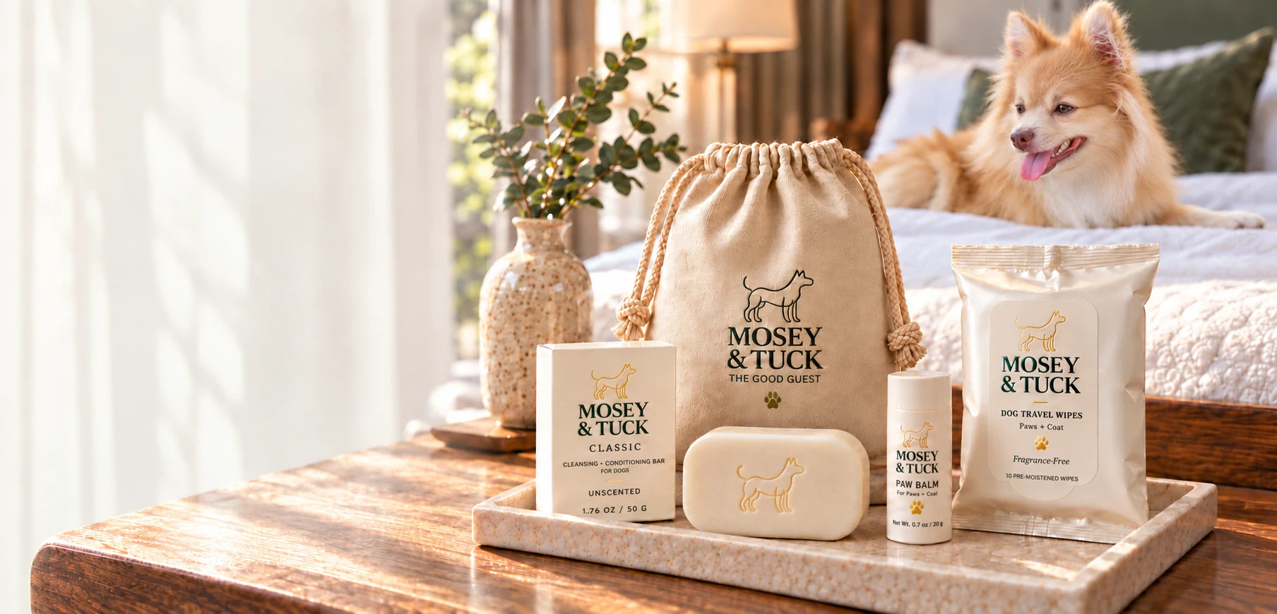 The Good Guest kit on a hotel-room tray, with Archie resting on the bed behind it