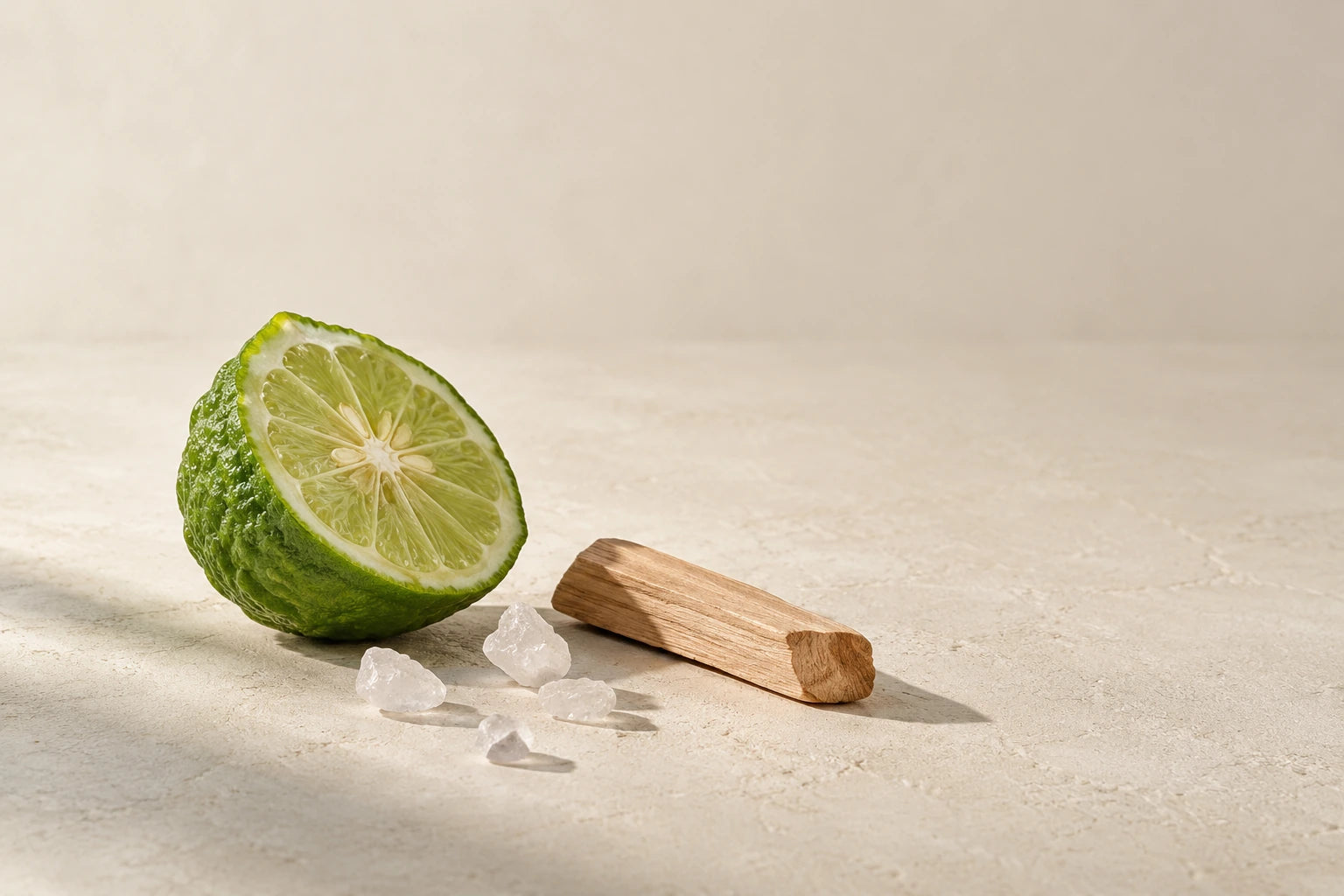 A cut bergamot, a few sea salt crystals and sandalwood in a minimal ivory studio still life